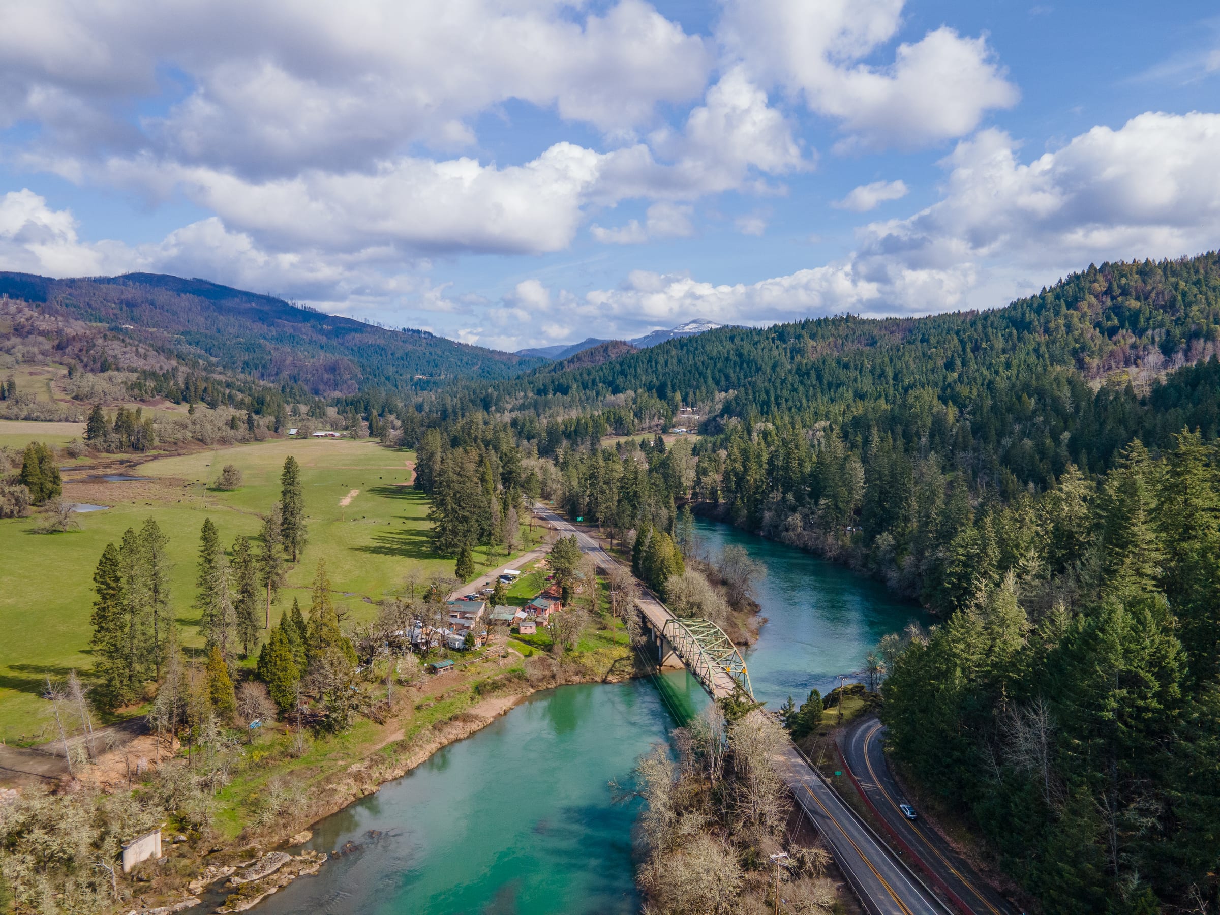 The green North Umpqua River winding past Glide in March, fields and wooded hills under white clouds