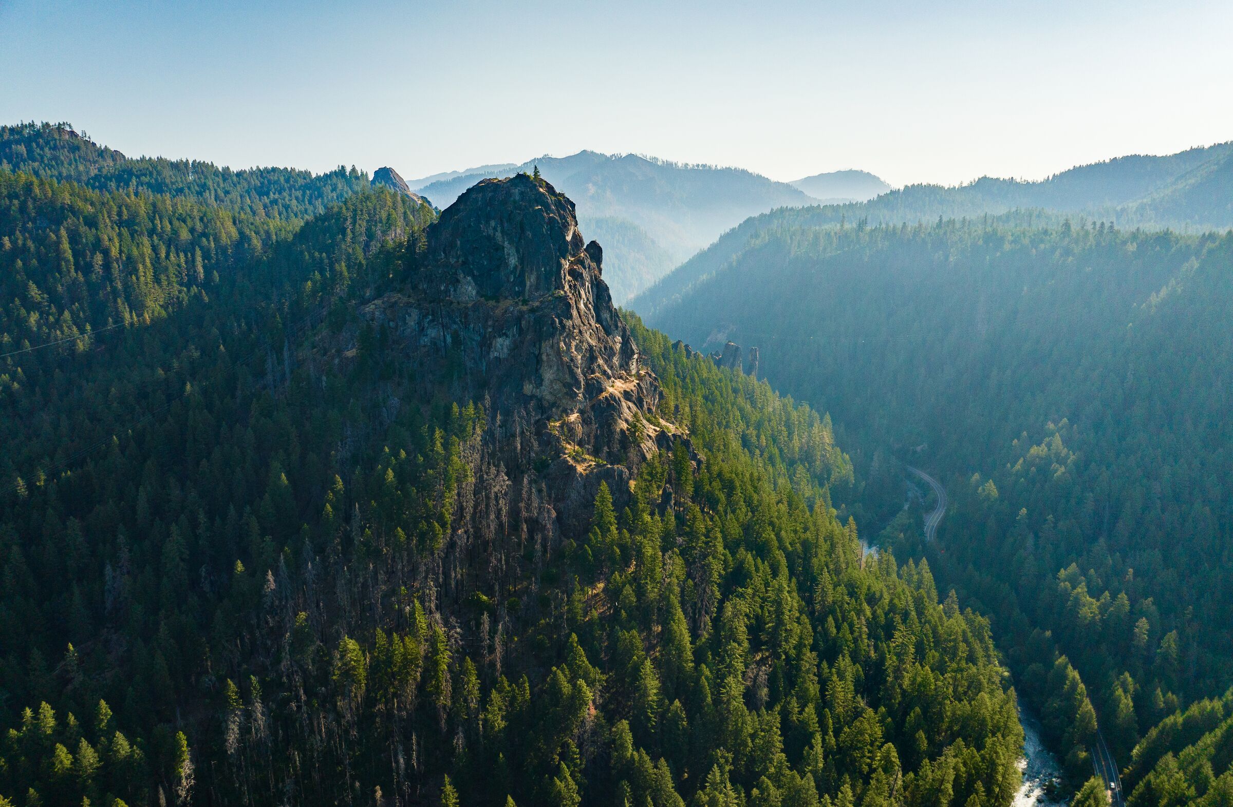 A rock peak on a forested ridge above the deep canyon of the North Umpqua River, more ridges fading into August haze