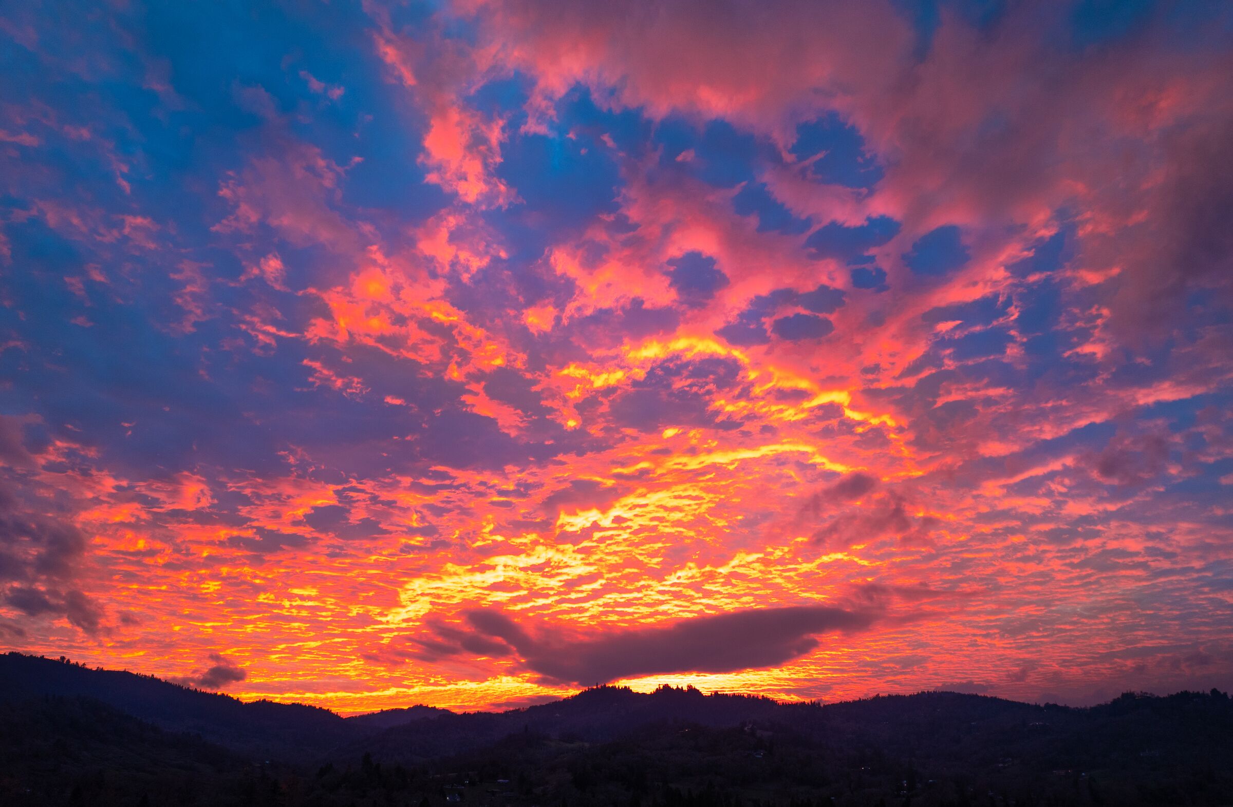 Red and pink December sunset clouds over the dark hills and fields outside Roseburg
