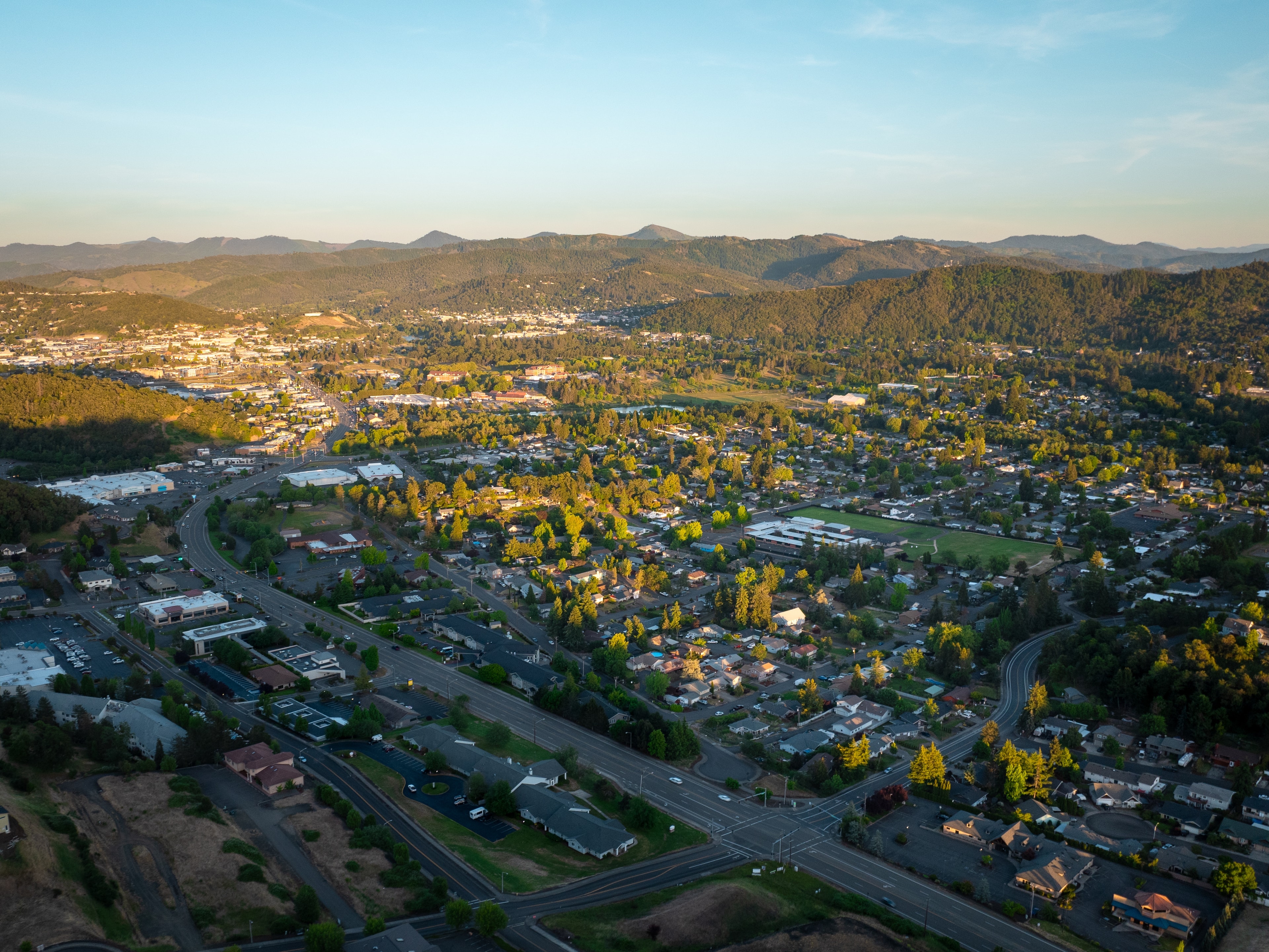 Roseburg from the air on a May evening, streets, parks and green trees in low light under the hills