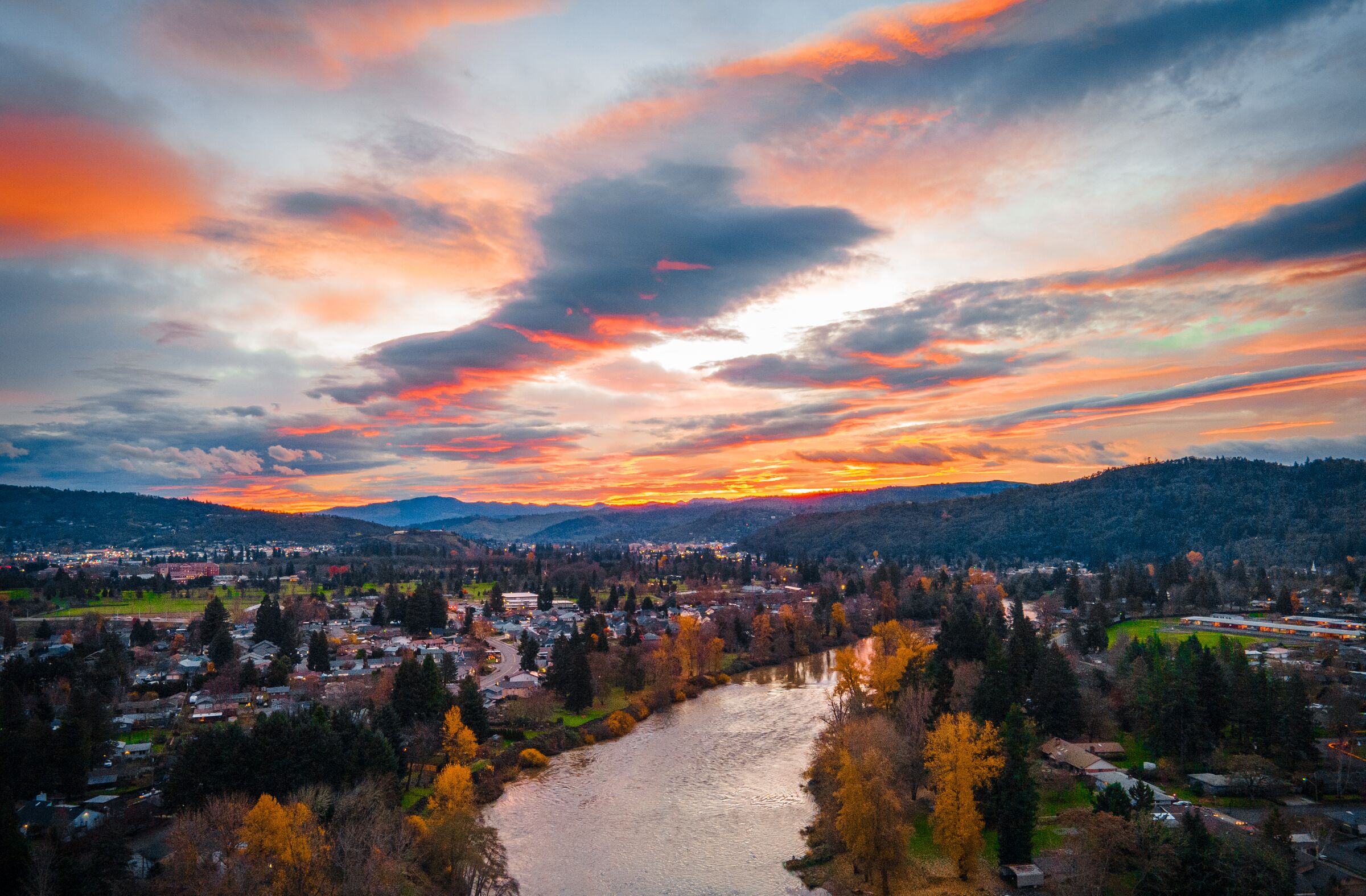 The South Umpqua River through Roseburg under an orange and pink December sunrise, yellow trees along both banks and hills beyond