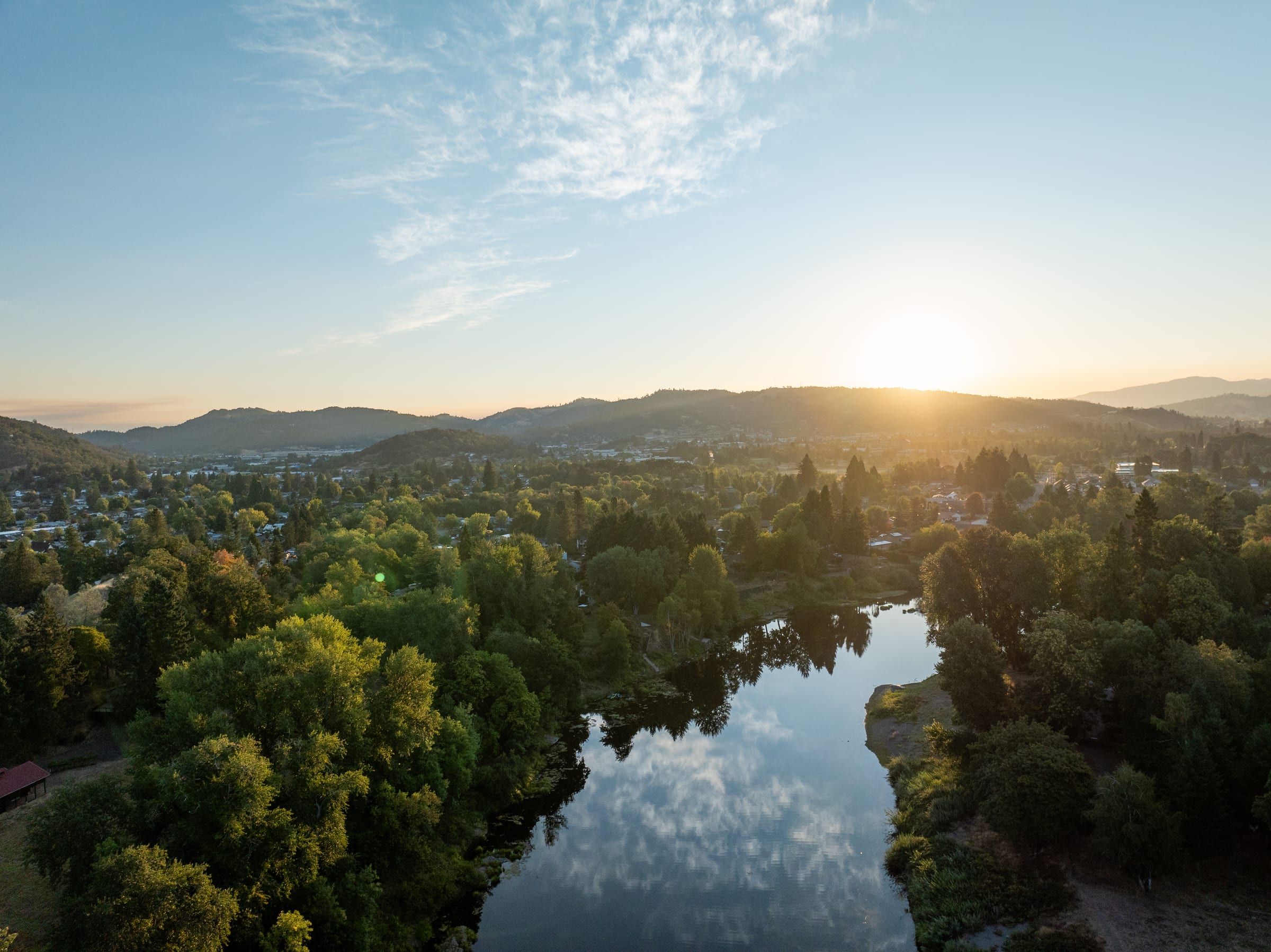 The sun rising over the hills behind Roseburg, the South Umpqua River reflecting the sky between tall trees